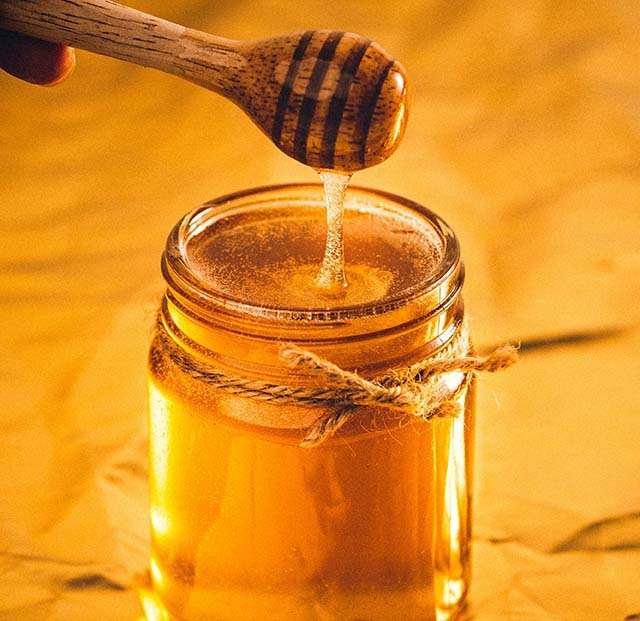 honey drizzling from a dipper into a jar